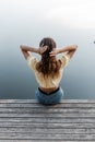 Young woman in fashion blue jeans and a yellow blouse straightens her hair and sits on a wooden pier near the lake Royalty Free Stock Photo