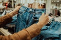 Young woman in fashion store chooses things for herself - jeans, denim trousers. Customers, shopping, sales concept. Royalty Free Stock Photo