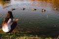 Young woman feeding ducks while sitting by the lake during sunny weather Royalty Free Stock Photo