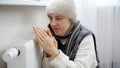 Young woman feeling cold in house sitting at heating radiator. Concept of energy crisis, high bills, broken heating system, Royalty Free Stock Photo