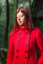 Young woman feeling sad walking alone on forest path wearing red long coat Royalty Free Stock Photo