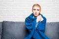 Young woman feeling sick or sad wrapped in cozy blue blanket and sitting on sofa at home Royalty Free Stock Photo