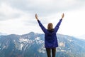 A young woman feels strong and raised her hands up, enjoys a beautiful mountain landscape