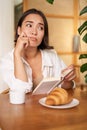 Young woman feels uneasy, reads sad book and sits in cafe with cup of coffee, looks around with sulking unhappy face Royalty Free Stock Photo