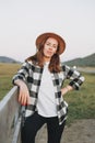 Young woman in felt hat and plaid shirt near old wooden fence on the mountains background Royalty Free Stock Photo