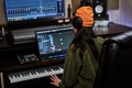 Young woman, female artist looking focused while playing keyboard synthesizer, sitting in recording studio