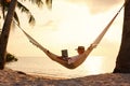 Young woman female freelancer using laptop while lying in hammock on the tropical beach at sunset Royalty Free Stock Photo