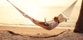 Young woman female freelancer using laptop while lying in hammock on the tropical beach at sunset