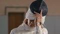 A young woman fencer with long hair takes off the helmet