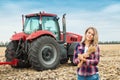 A young woman in a field on a background of a tractor with spike of wheat in her hands