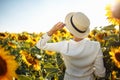 Young woman in a field of sunflowers stands back and looks at the sunset feeling freedom and joy. Female wearing a white Royalty Free Stock Photo