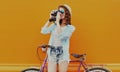 Young woman with film camera and bicycle on an orange background