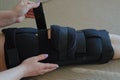 Young woman fixing adjustable orthosis on broken leg sitting in bed. Wearing leg brace after injury