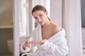 Young woman with flawless skin, applying moisturizing cream on her face. Photo of woman after bath in white bathrobe and towel on Royalty Free Stock Photo