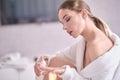 Young woman with flawless skin, applying moisturizing cream on her face. Photo of woman after bath in white bathrobe and towel on Royalty Free Stock Photo