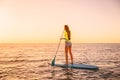 Young woman floating at stand up paddle board with warm sunset colors Royalty Free Stock Photo