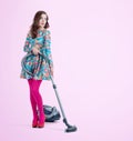 Young woman in a floral dress in red heels with a vacuum cleaner on pink background. Cleaning concept