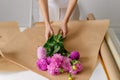 A young woman florist collects a bouquet of pink dahlias in brown kraft paper. Horizontal image for your design