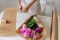 A young woman florist collects a pink bouquet of dahlias in brown kraft paper and ties it with a tourniquet. Image for your design