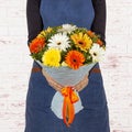 Young woman florist holding big beautiful blossoming bouquet of yellow, orange and white flowers in blue paper cone over Royalty Free Stock Photo