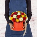 Young woman florist holding big beautiful blossoming red, white and yellow roses in red cardboard round box over white Royalty Free Stock Photo