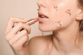 Young woman with flowers on face applying lipstick against light background, closeup Royalty Free Stock Photo