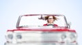 A young woman with fluttering hair rides in a red toy convertible, front view, on a light blue background