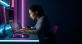 Female programmer working on laptop and desktop monitors in dark room with neon lights coding software development and cyber Royalty Free Stock Photo