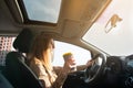 Young woman focused on driving holds a cup of coffee or tea . Sun rays on the windshield. Driving concept Royalty Free Stock Photo