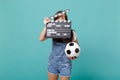 Young woman football fan with soccer ball, covering face with classic black film making clapperboard isolated on blue Royalty Free Stock Photo