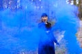 Young woman in forest having fun with blue smoke grenade, bomb Royalty Free Stock Photo