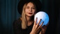 A young woman fortune teller in a hat is holding a magic ball. Royalty Free Stock Photo