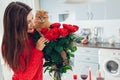 Young woman found red roses with candle, wine and gift box on kitchen. Happy girl smelling flowers with cat Royalty Free Stock Photo