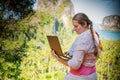 Young woman freelancer in white working with laptop on a top of the mountain with view on sea and tropical beach. Work and travel Royalty Free Stock Photo