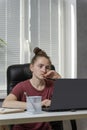 Young woman freelancer works from home. Girl sits at the workplace, works at laptop, tired of taking up her head. Vertical frame