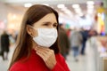 Young woman with a frowning face holds her throat and wears a protective mask while shopping at the Mall. Royalty Free Stock Photo