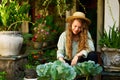 Young woman gardener holding gardening trowel in straw hat taking care of green potted plants. Junior caucasian female