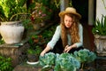 Young woman gardener holding gardening trowel in straw hat taking care of green potted plants. Junior caucasian female