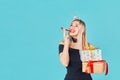 Young woman with gift box and blowing party horn or noisemaker while celebrating birthday on blue background Royalty Free Stock Photo