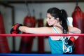 A young woman girl is hanging on the ropes of a boxing ring, resting, wearing boxing gloves. Royalty Free Stock Photo