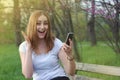 Young women Girl Happy with Smartphone on Hand. girl gets Good News. Blured Green Garden Park. Blonde Girl.