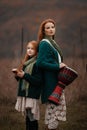 A young woman and a girl with red long hair playing kalimba and drum in the mountains in autumn Royalty Free Stock Photo