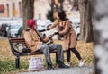 Young woman giving food to homeless beggar man sitting on a bench in city.