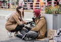 Young woman giving money to homeless beggar man sitting in city. Royalty Free Stock Photo