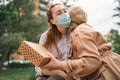 Young woman giving present and hugging grandmother outdoors in city, life after covid-19 vaccination. Royalty Free Stock Photo