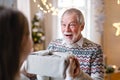 Young woman giving present to surprised grandfather indoors at home at Christmas.