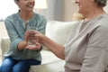 Young woman giving water to elderly lady indoors. Senior people care Royalty Free Stock Photo