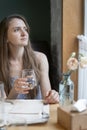 Young woman with glass of water sits at table in cafe and looks out the window waiting for an order. Portrait of girl in cafe Royalty Free Stock Photo