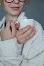 Young woman in glasses get warm by drinking hot tea closeup, gray background, free copy space. Cozy white sweater, shirt Royalty Free Stock Photo