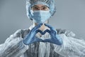 Young woman in glasses with a medical mask and hands in latex glove shows the symbol of the heart